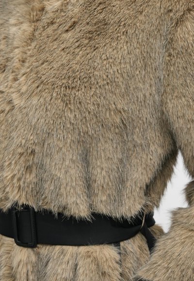 Abrigo de piel sintética en beige con un acabado suave y texturizado. Cuenta con un cinturón negro en la cintura y un diseño de corte holgado.