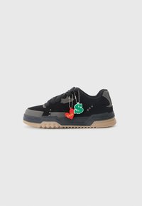 Black and gray sneaker with a tan rubber sole, thick laces, and two decorative charms: a red heart labeled "Devil" and a green dollar sign.