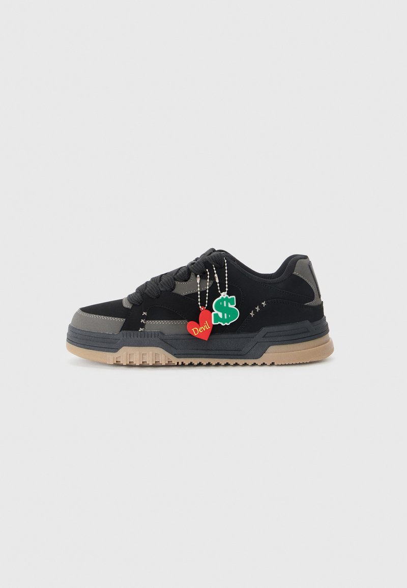 Black and gray sneaker with a tan rubber sole, thick laces, and two decorative charms: a red heart labeled "Devil" and a green dollar sign.