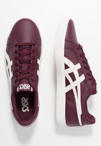 Sneakers in pelle bordeaux con strisce e lacci bianchi, caratterizzati da un rivestimento testurizzato e una suola in gomma bianca a contrasto.