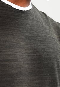 Dunkelgraues, strukturiertes Strickshirt mit Rundhalsausschnitt und kontrastierendem weißen Innenkragen. Glatter Stoff mit subtilen horizontalen Streifen.