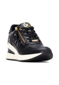 Zapatilla negra con textura acolchada y suave, que presenta herrajes dorados, un zipper lateral y una suela de cuña blanca para mayor altura.