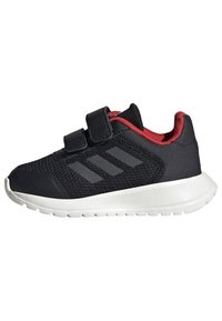 Černá sportovní bota s červenými akcenty, svrchní část z prodyšné síťoviny, dvě suché zipy, šedé logo se třemi pruhy a bílá gumová podrážka. Nízkoprofilový design.