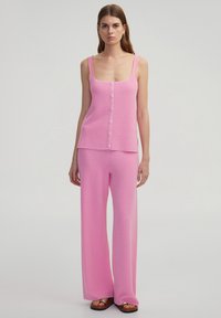 Rosa gestricktes Zweiteiler-Outfit mit einem ärmellosen Oberteil mit Knopfverschluss und weit geschnittenen Hosen. Texturiert Stoff mit einem lässigen Design.