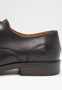 Chaussure en cuir noir au cuir lisse, au design arrondi et à l'intérieur marron. Présente un talon en bois et des détails de couture subtils.