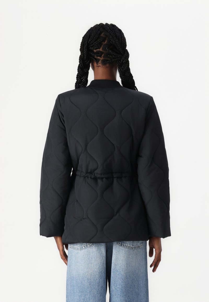 Schwarze gesteppte Jacke mit einem wellenmuster, die eine taillierte Taille und einen gerippten Kragen aufweist. Lange Ärmel und eine lockere Passform rundet das Design ab.