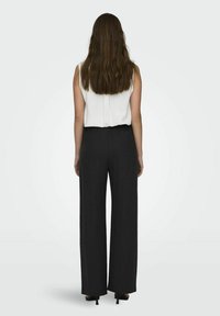 Schwarze weite Hosen mit elastischem Bund, kombiniert mit einem ärmellosen weißen Oberteil, von hinten betrachtet, mit glatten Texturen.