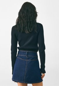 Čierny rebrovaný top s dlhým rukávom v kombinácii s tmavomodrou rifľovou sukňou, ktorá má vysoký pás a viditeľné švy.