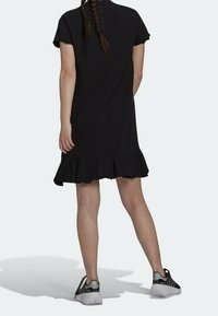 Černé šaty s krátkým rukávem a volánkovým lemem, vyrobené z měkké látky. Mají vysoký výstřih a jemný zadní zip. Spárováno se sportovními botami.