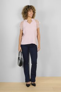 Top rosa chiaro con maniche in pizzo, design a V, abbinato a jeans blu scuro e décolleté neri a punta. Tiene una borsa nera.