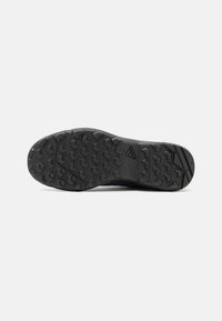 Black athletic shoe sole with a textured tread pattern, featuring a logo. The shape is curved with a wider heel section for stability.