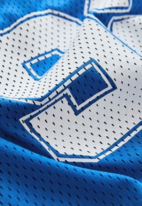 Tissu de maillot de sport bleu avec un grand numéro blanc perforé entouré de bleu, montrant une texture courbée et pliée.