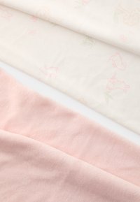 Due strati di tessuto: un materiale morbido e rosa in basso e uno strato crema sopra con sottili motivi pastello di conigli e fiori.