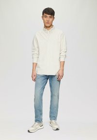 Witte gestreepte button-up shirt, lichtblauwe jeans en grijze sneakers met groene accenten. Het shirt heeft opgerolde mouwen en een kraag.