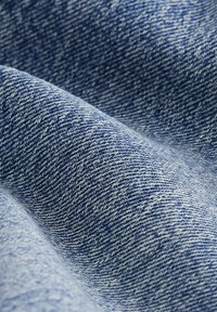 Gros plan sur un tissu en denim bleu montrant une texture de tissage diagonal et des plis subtils.