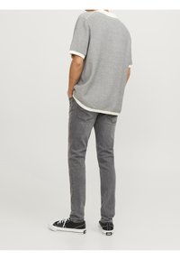 Camisa de manga corta a rayas en gris y blanco, combinada con jeans grises y zapatillas negras. La camisa presenta un cuello y puños en contraste.