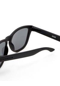 Schwarze Sonnenbrille mit matter Oberfläche, runden Gläsern, dicken Rahmen und eleganten, geschwungenen Bügeln. Verfügt über eingravierten Markentext an den Bügeln.