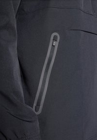 Zwarte waterdichte jas met een ritszak en een grijze accent, gladde textuur en minimalistisch ontwerp.