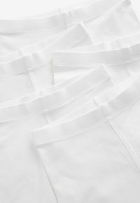 Paquet de quatre slips en coton blanc avec une taille élastique douce, présentant une texture lisse et un design simple. Aucun motif ni accent présent.