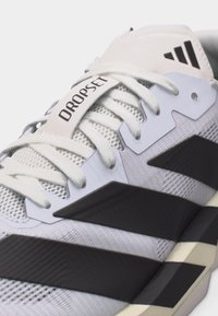 Κοντινό πλάνο λευκού και μαύρου παπουτσιού Adidas Dropset με κορδόνια, υφασμάτινο επάνω μέρος και λογότυπο στη γλώσσα και τις πλαϊνές ρίγες.