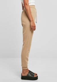 Lys beige joggebukser med tapered ben, elastisk midje, snor, og sidelommer; kombinert med svarte platåsandaler.