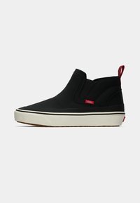 Black Vans slip-on sneaker with white sole, red logo tag on side, and red checkered pull tab on heel.