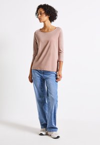 Ljusrosa långärmad topp med båturringning, kombinerad med löst sittande ljusblå jeans och vita sneakers. Slät tyg, avslappnad design.