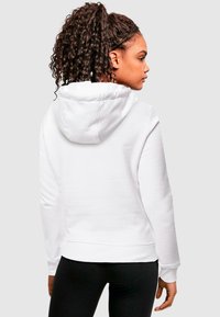 Fehér kapucnis pulóver, húzózsinórral, hosszú ujjakkal, bordázott mandzsettákkal és alsó résszel. Puha szövettextúra látható. Fekete leggings-szel viselve.