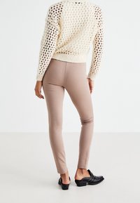 Beige leggings med en tight passform, kombinerat med en texturerad krämfärgad tröja med diamantmönster och ribbad midja. Svarta klackskor i mule-stil.