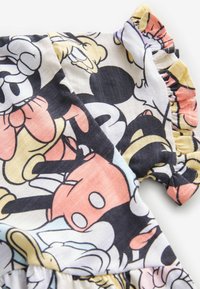 Gros plan sur un tissu avec un imprimé cartoon coloré de Mickey Mouse et un bord froncé sur un fond clair.