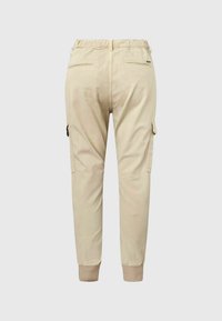 Beige cargo kalhoty s elastickými manžetami, bočními kapsami na klopu a zadními kapsami s lemováním, zobrazené zezadu na jednobarevném pozadí.