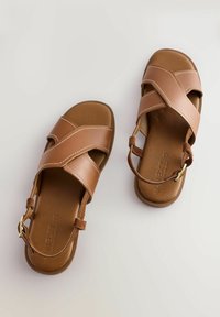 Sandali in pelle marrone con fasce incrociate, soletta imbottita e cinturino alla caviglia regolabile. Presentano cuciture bianche e una suola piatta.