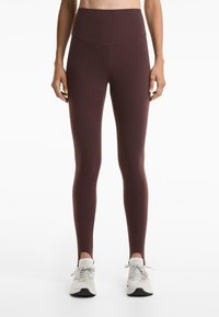 Maroon high-waisted leggings made from stretchy fabric; features a smooth texture and no visible seams. Worn with white athletic shoes.