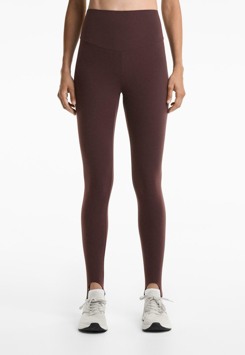 Maroon high-waisted leggings made from stretchy fabric; features a smooth texture and no visible seams. Worn with white athletic shoes.