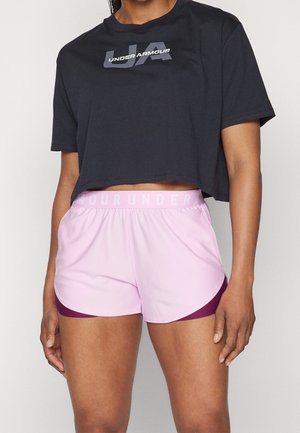 Vrouw draagt een zwart cropped Under Armour T-shirt en lichtroze sportshorts met bordeauxkleurige afwerking en elastische tailleband.