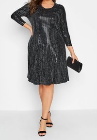 Svart klänning med trekvartslånga ärmar, dekorerad med paljetter, utsvängd kjol och rund halsringning. Matchad med en svart clutchtaska och remsandaler.