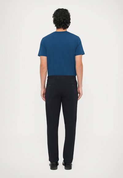 Tricou din bumbac albastru marin cu gât rotund, asortat cu pantaloni închiși la culoare. Ținuta are o croială lejeră și detalii minimale.