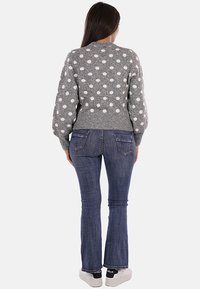 Maglione grigio lavorato a maglia con pois bianchi, design cropped e orlo a costine; abbinato a jeans svasati blu e sneakers bianche.