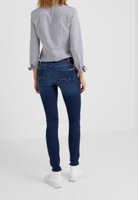 Jeans ajustados de color azul oscuro con una textura suave, que cuentan con bolsillos traseros con costuras en contraste y una camisa de rayas con cuello blanco.