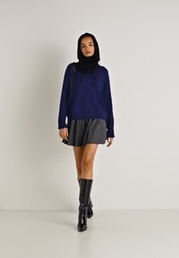 Tengerészkék kapucnis, hosszú ujjú pulóver, szürke, pliszírozott mini szoknyával és térd fölé érő, fekete, fényes csizmával párosítva. Egyszerű, modern dizájn.