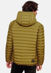 Olivengroene pufferjack met horizontale stiksels, een capuchon en een klein zwart label aan de zoom, met een gladde, gequiltte textuur.
