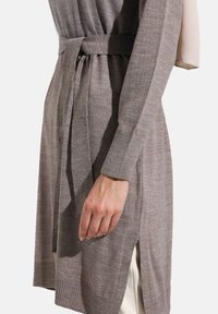 Long, light gray cardigan made of soft knit fabric. Features a tie belt, ribbed cuffs, and side slits for ease of movement.
