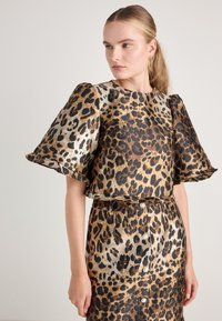 Leopardmønstret todelt antrekk inneholder en kortermet, cropped topp med voluminøse ermer og et matchende blyantskjørt med belte i midjen.
