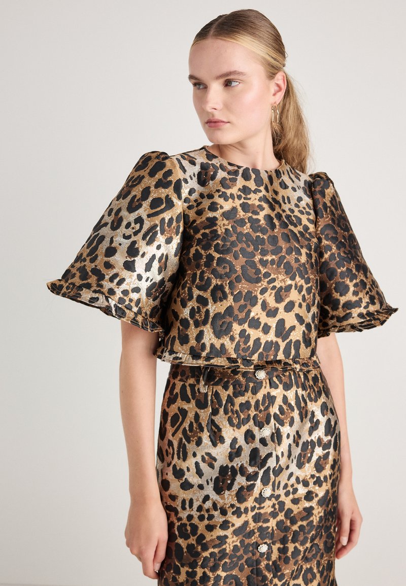 Leopardmønstret todelt antrekk inneholder en kortermet, cropped topp med voluminøse ermer og et matchende blyantskjørt med belte i midjen.