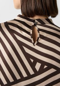 Bluza z nadrukiem w brązowo-beżowy paski, z otworem w kształcie dziurki na plecach, zamkniętym małym czarnym guzikiem.