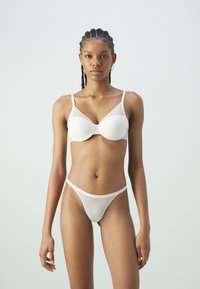 White wireless bra and matching thong, featuring seamless design, textured fabric, and thin straps. Minimalist style with geometric pattern.