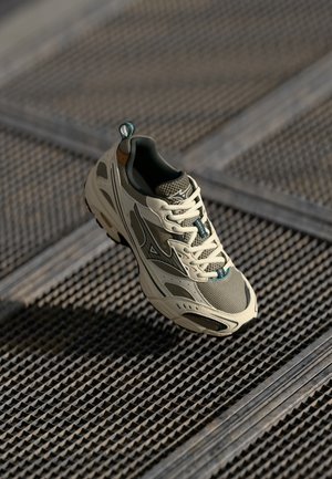 Lightweight beige athletic shoe with mesh fabric, green accents, and cushioned sole. Features a textured design and a pull tab at the heel.