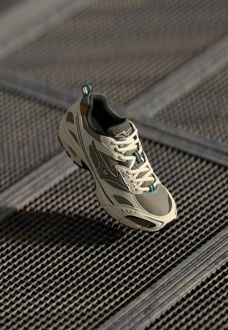 Scarpa atletica leggera beige con tessuto a rete, dettagli verdi e suola imbottita. Presenta un design testurizzato e una linguetta sul tallone.