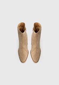 Stivaletti beige in suede con punta affilata, dotati di zip laterale, texture liscia e tacco basso impilato.