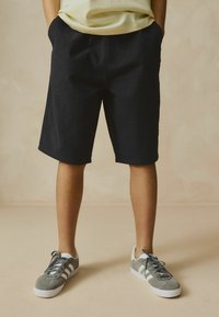 Shorts noirs texturés avec poches latérales, associés à des baskets en suède grises avec des rayures blanches. La tenue a une coupe décontractée.